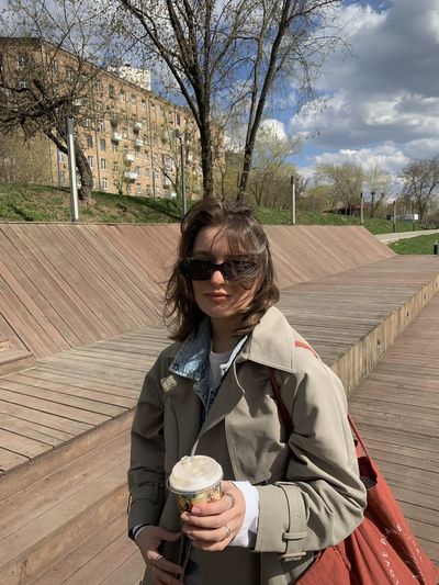 Young woman using mobile phone and drinking coffee in park 