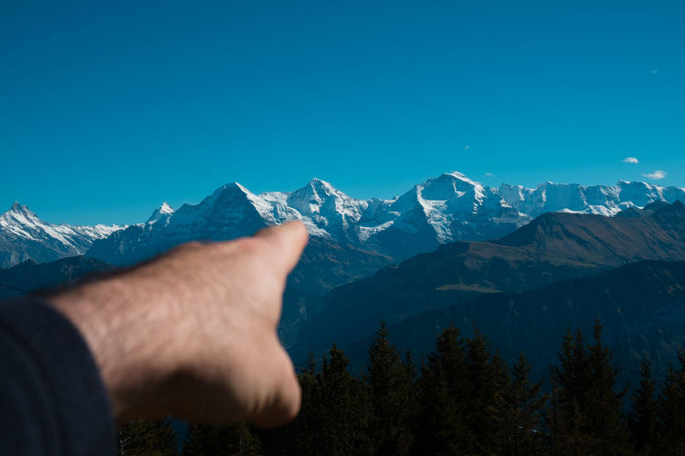 Cropped hand of man pointing at snowcapped mountains