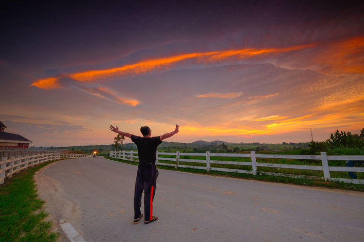 Rear view of man standing on street against sky during sunset