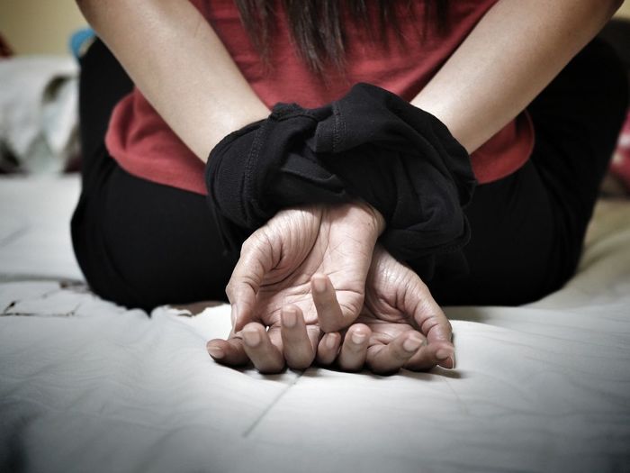 Midsection of woman with tied hands on bed at home
