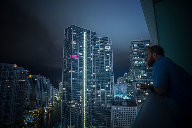Man standing in balcony against buildings in city at night