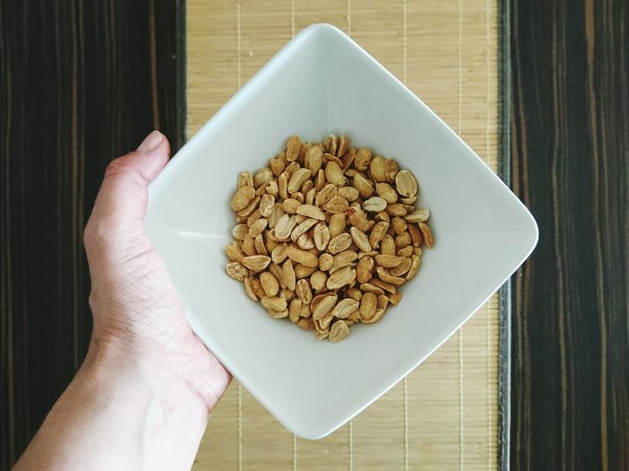 Cropped hand holding peanuts in bowl over table