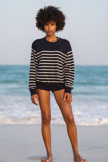 Young black woman standing by the sea wearing striped jumper