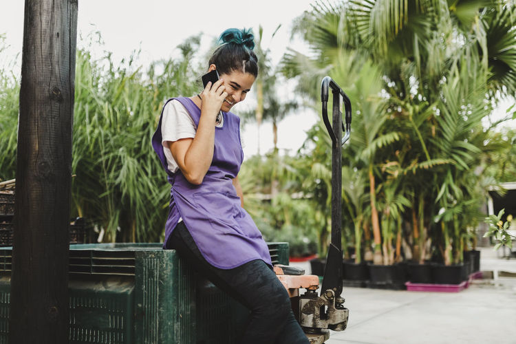 Happy female owner talking on smart phone in garden center