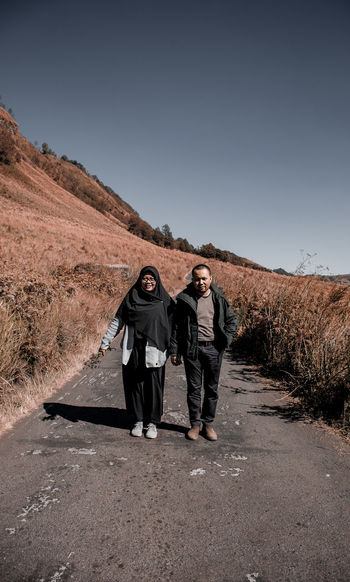 Portrait of couple walking on road against sky