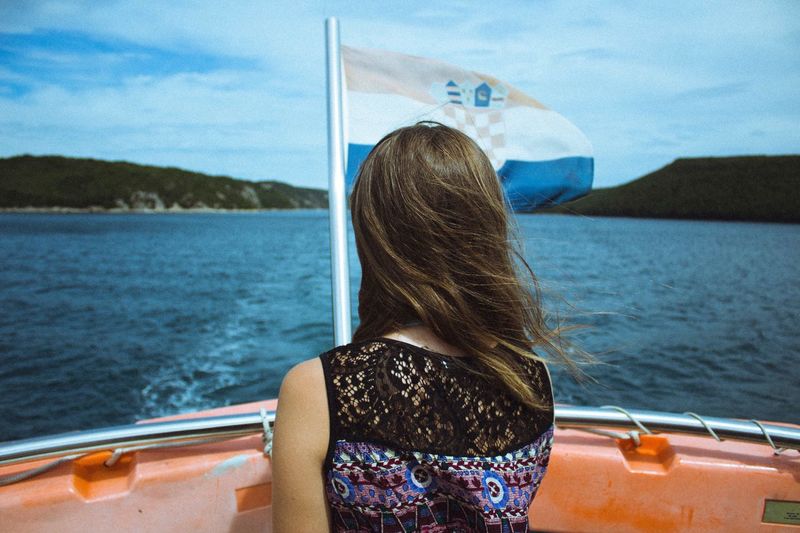 Rear view of woman by croatian flag in boat on lake