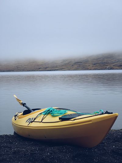 Kayak moored by river against sky