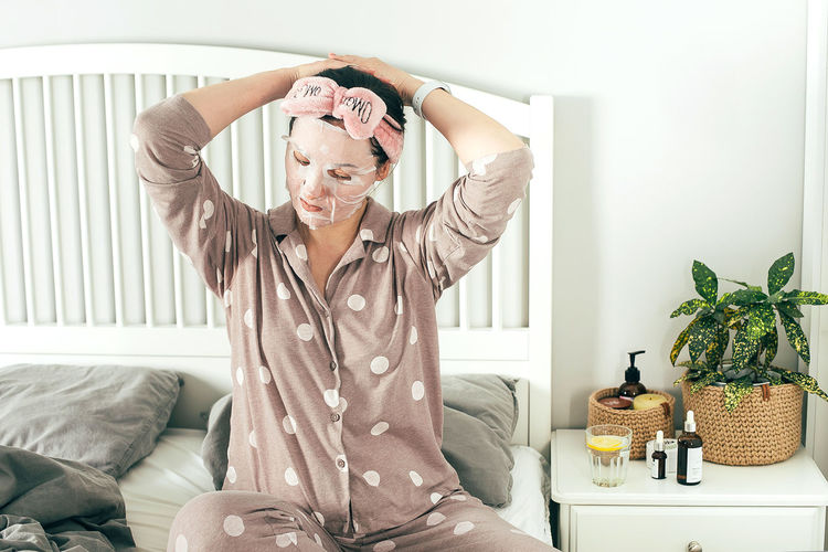 Woman with face mask while sitting on bed at home