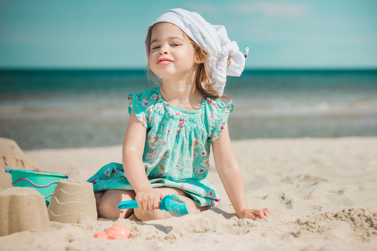 Portrait of girl making sandcastles while sitting at beach