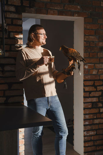 Man drinking coffee with wild bird at home on the kitchen in morning. eagle as pet. unusual animals