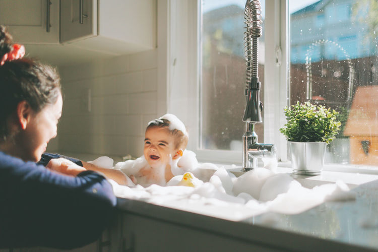Cheerful baby boy in bathtub looking at mother
