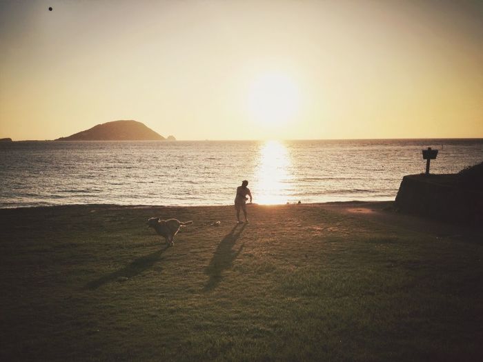 Man playing with dog on sea shore against sky during sunset