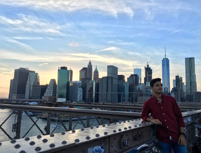 Young man standing on brooklyn bridge against urban skyline during sunset