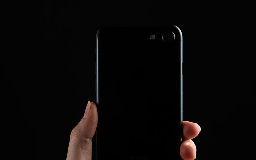 Cropped hand of person using smart phone against black background