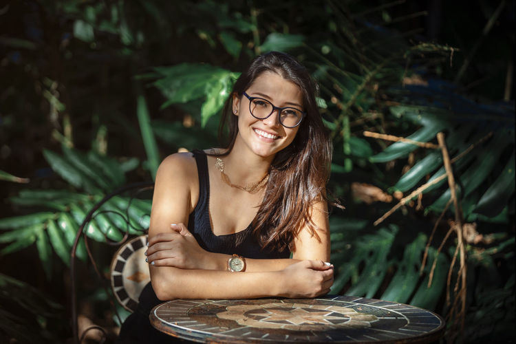 Beautiful young latina woman sitting at a table with jungle type background