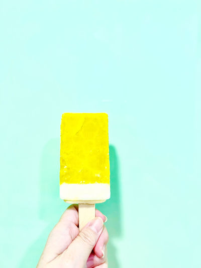 Cropped hand holding ice cream against blue background