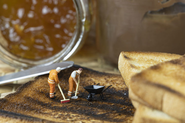 Miniature people are cleaning out burnt toast.