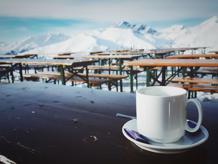 Coffee cup on table against mountains during winter