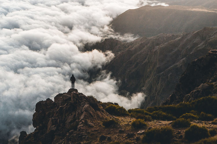 Person standing on mountain against clouds