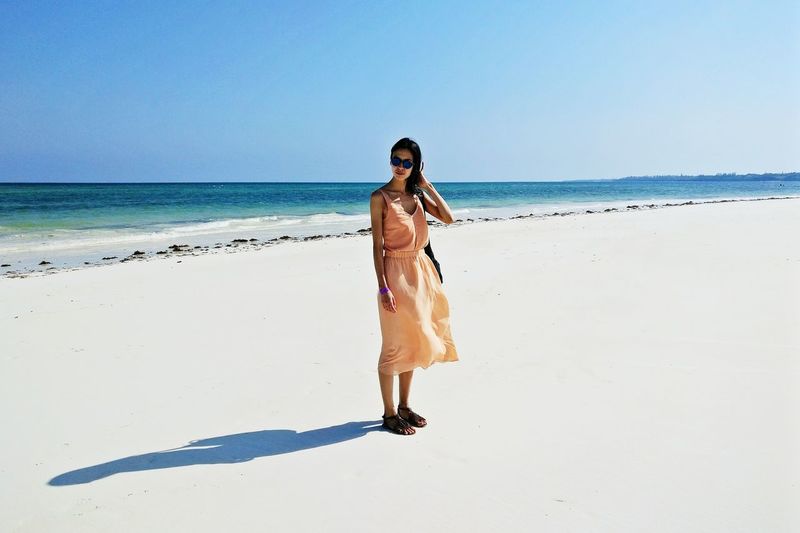 Full length of young woman standing on beach against clear sky
