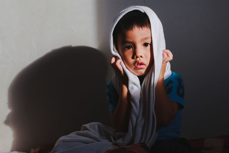Portrait of boy with towel on head sitting by wall