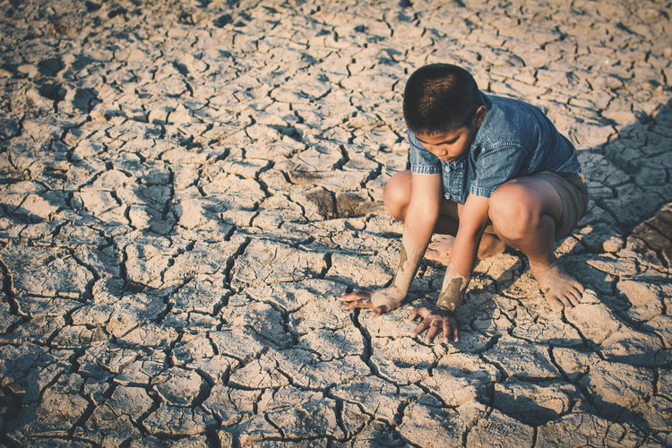 Full length of boy crouching on barren landscape
