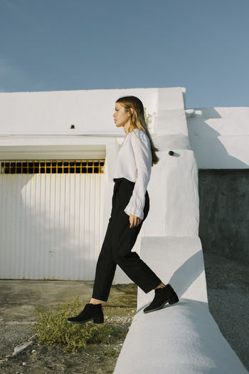 Side view of young blond lady in stylish clothes strolling above meadow while looking forward under blue sky