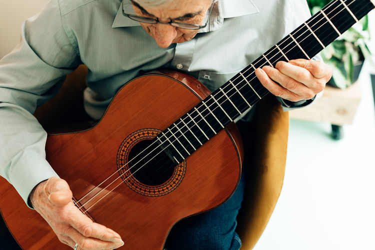 Elderly man playing on acoustic guitar at home. senior person with music hobby.