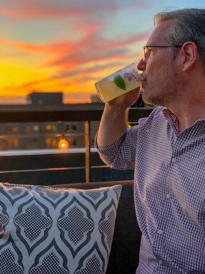Mature man having drink against sky during sunset