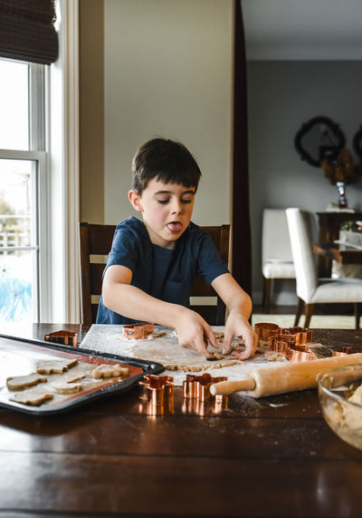 Young boy making cookies with cookie cutters at the table.