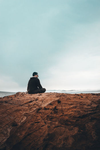 Rear view of man sitting on rock