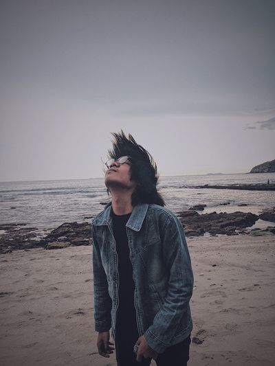 Man with tousled hair standing on shore at beach