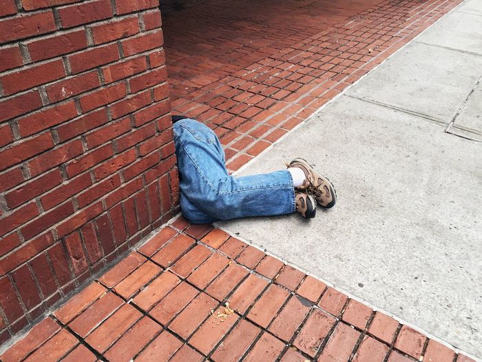 Low section of person sleeping by brick wall