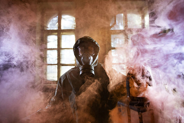 Portrait of woman holding oil lamp wearing gas mask standing amidst smoke