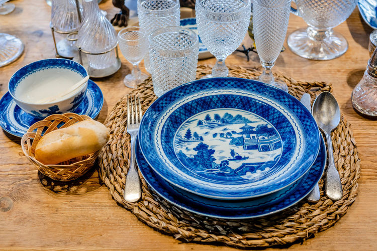 From above of blue ceramic plates served on wooden table with elegant glassware and silverware