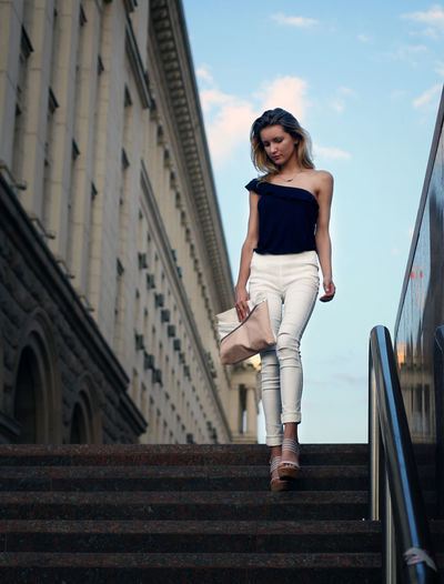 Young woman on staircase by building against sky