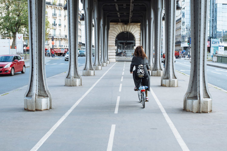 Rear view of woman riding bicycle under bridge