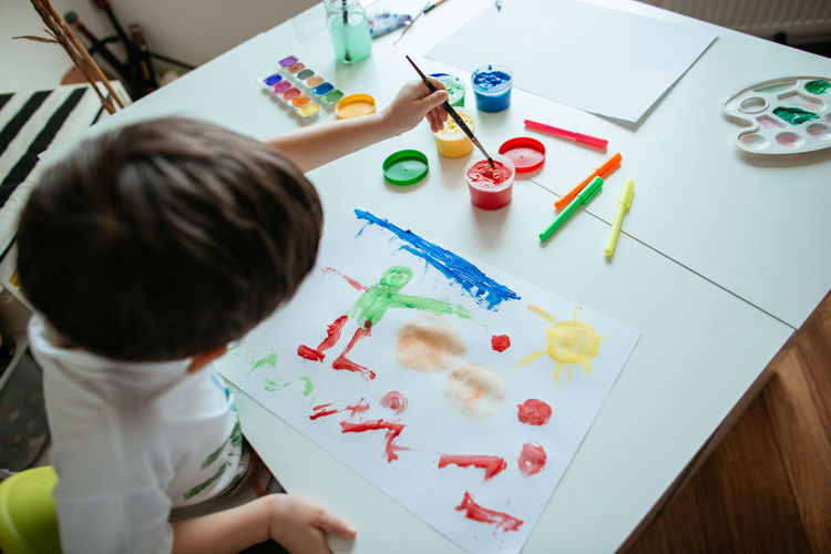 Directly above shot of boy doing painting while sitting at home