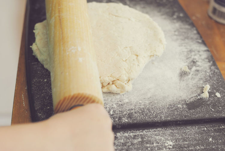 Cropped hand of woman pressing dough with rolling pin