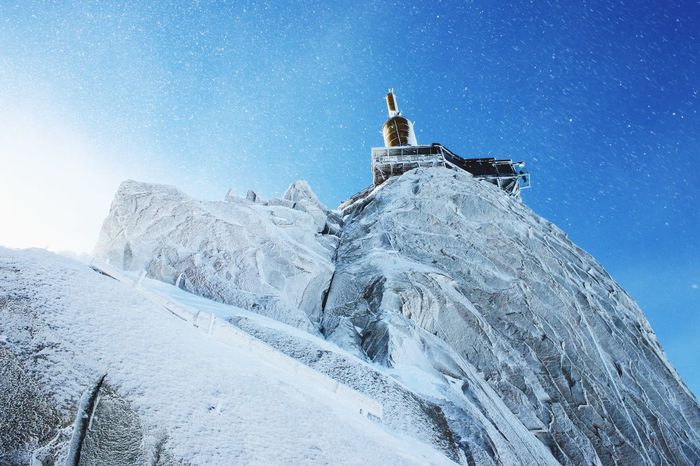 Low angle view of aiguille du midi in snow against blue sky