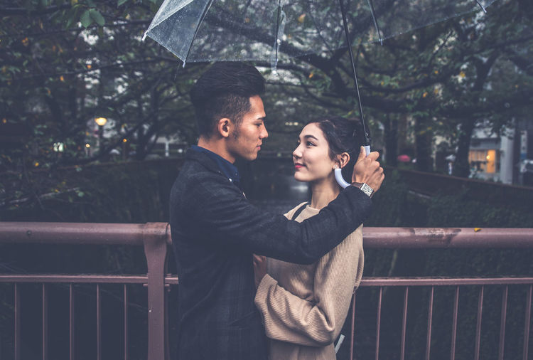 Couple holding umbrella standing by railing in city