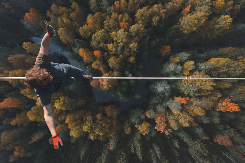 A breathtaking view of a tightrope walker walking along a line high above a beautiful forest. 