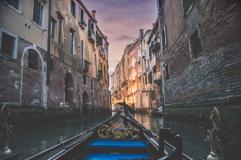 Gondola in canal amidst buildings during sunset