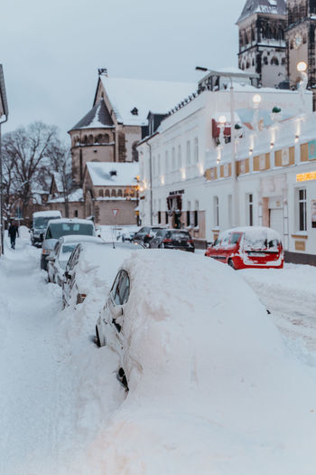Snow covered road and cars by buildings in city