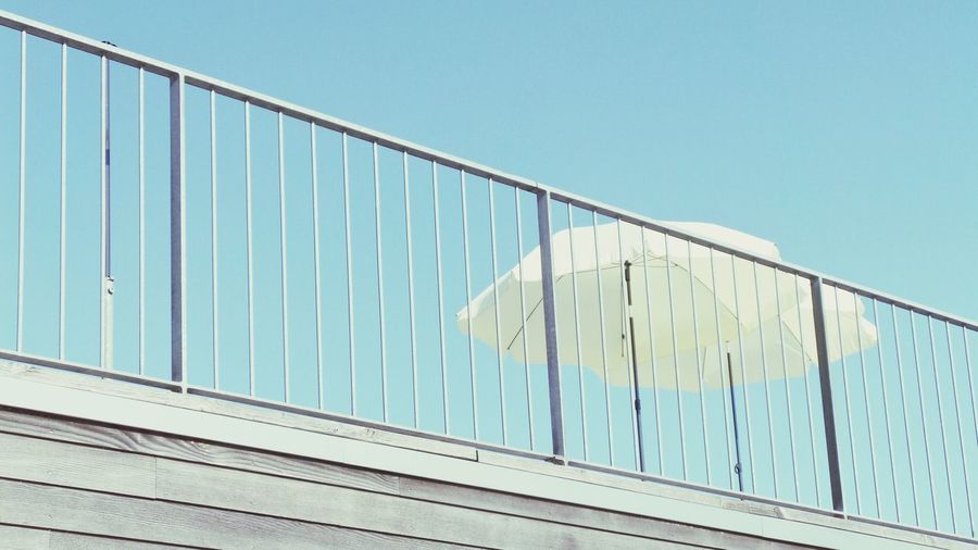 Low angle view of umbrella next to railing against clear sky
