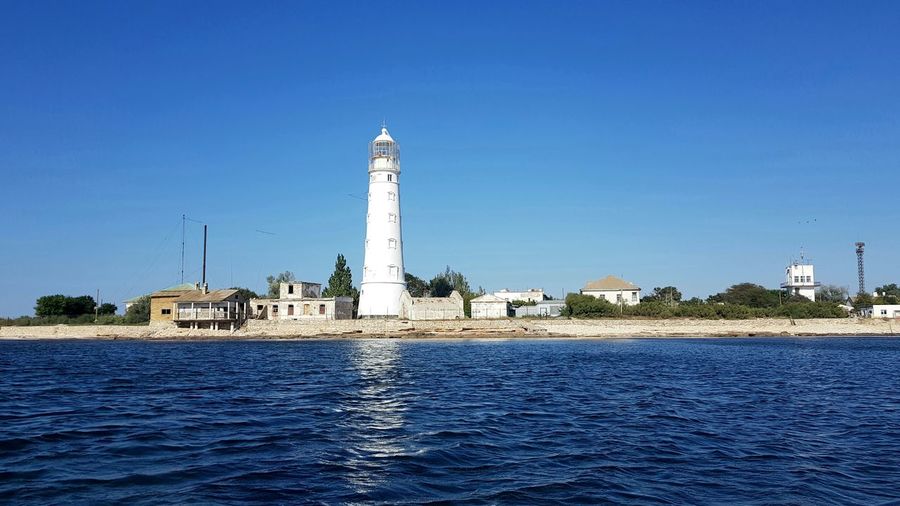Lighthouse on building by sea against clear blue sky
