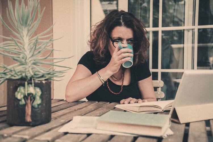 Young woman drinking water from coffee while sitting on table