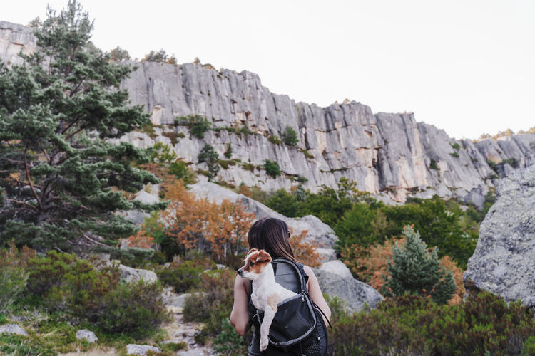 Woman carrying dog in backpack while hiking on mountain