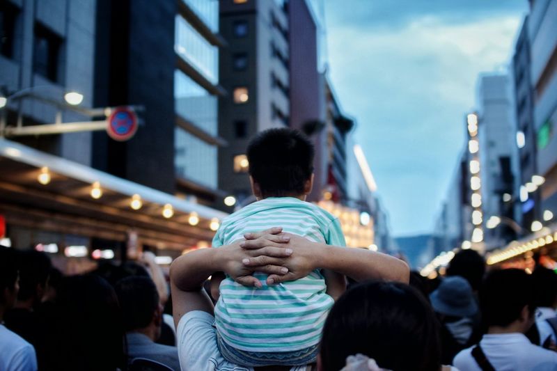 Rear view of father carrying son on shoulders on street at dusk