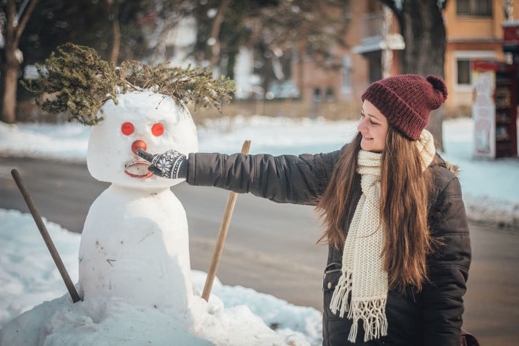 Smiling woman touching snowman in city